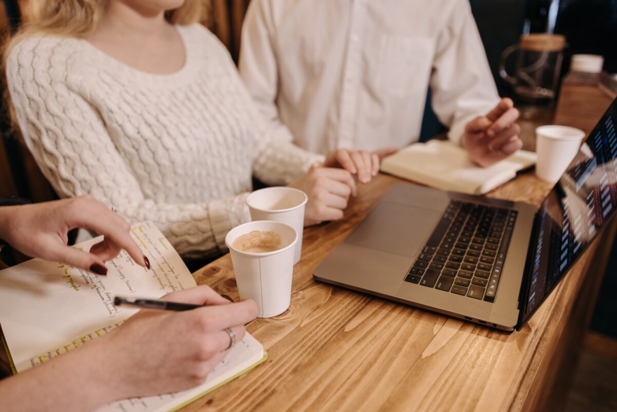 Trzech designerów siedzi w kawiarni i tworzy prototym aplikacji mobilnej na laptopie 